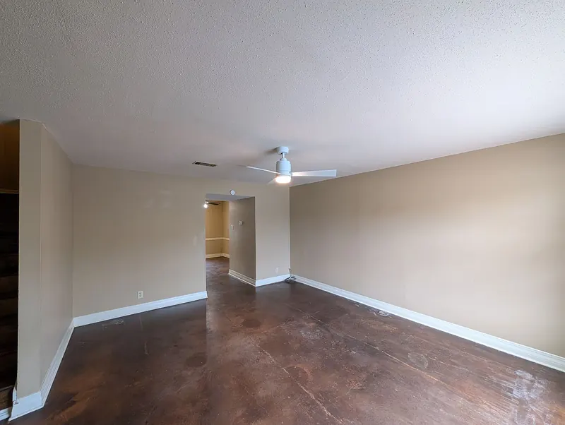 Living and dining area with stained concrete floors and a ceiling fan, looking toward the kitchen