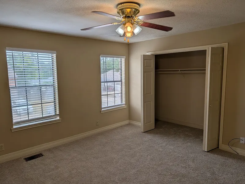 Bedroom with new carpet, ceiling fan, two windows, and an open closet
